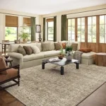 The image shows a luxurious, intricately patterned Persian rug in a well-decorated living room setting.