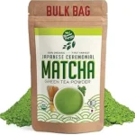 The image shows a vibrant green matcha tea being poured into a delicate ceramic bowl, contrasting with coffee in the background.